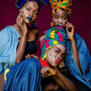Three women in colorful African outfits with face paint and headdresses celebrating culture.