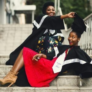 Two women in graduation gowns celebrating on stairs, embodying happiness and achievement.