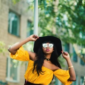 Fashionable woman in yellow top and hat striking a pose outdoors, showcasing vibrant urban style.